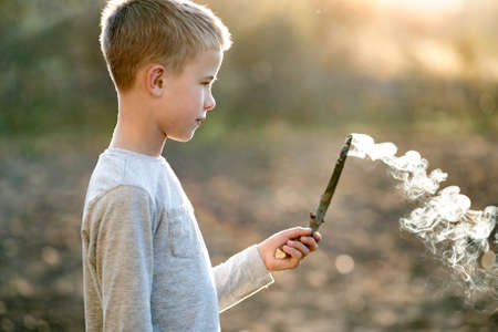 Child boy playing with smoking wooden stick outdoors.の写真素材