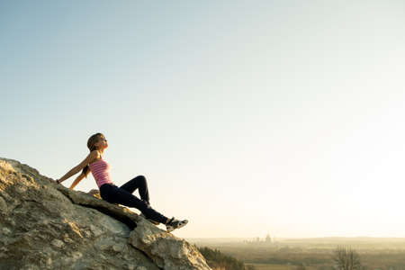 Woman hiker sitting on a steep big rock enjoying warm summer day. Young female climber resting during sports activity in nature. Active recreation in nature concept.の写真素材