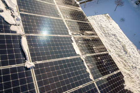 Close up surface of a house roof covered with solar panels in winter with snow on top. Energy...
