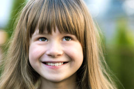 Portrait of pretty child girl with gray eyes and long fair hair smiling outdoors on blurred green...