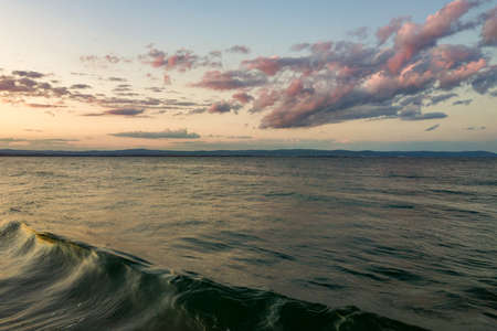 Sea surface with blue water waves under yellow and purple sunset sky.