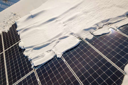 Close up surface of a house roof covered with solar panels in winter with snow on top. Energy...