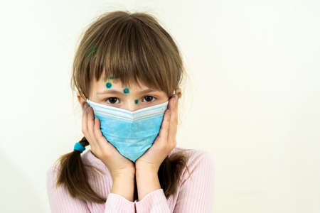 Child girl wearing blue protective medical mask ill with chickenpox, measles or rubella virus with...