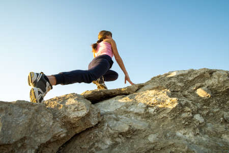 Woman hiker climbing steep big rock on a sunny day. Young female climber overcomes difficult climbing route. Active recreation in nature concept.の写真素材