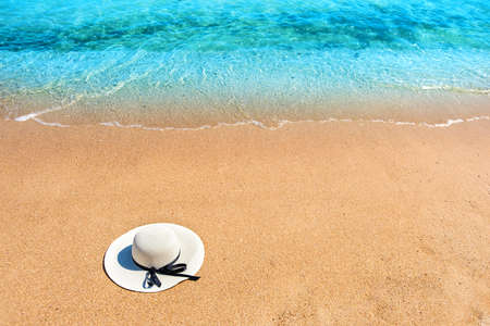 White woman straw hat laying on tropical sand beach with blue vibrant ocean water in background on...