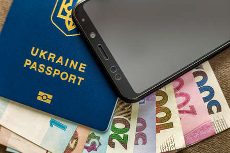 Modern black cellphone, money hryvnia banknotes bills and ukrainian travel passport on copy space background. Travelling light, comfortable journey concept.の写真素材