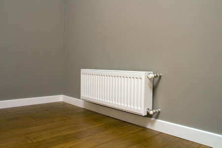 White metal heating radiator mounted on gray wall inside a room.