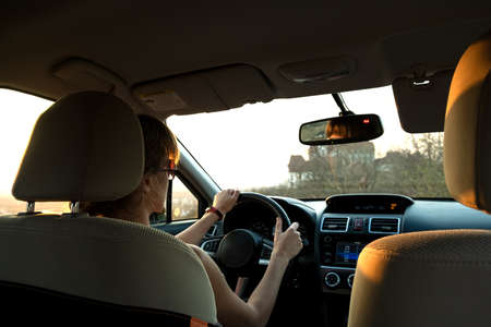 Close up view of a woman driver holding steering wheel driving a car at sunset.