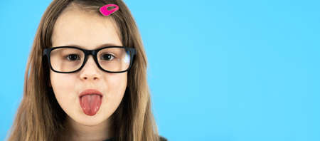 Close up portrait of a funny child school girl wearing looking glasses isolated on blue background.