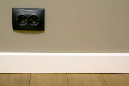 Close up of white plastic plinths on dark wooden oak floor parquet and black electric socket mounted...