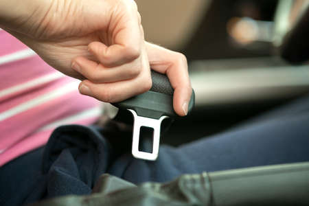 Close up of woman hand fastening seat belt while sitting inside a car for safety before driving on the road. Female driver driving secure and taking safe jorney.の写真素材