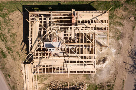 Aerial view of unfinished brick house with wooden roof frame structure under construction.の写真素材