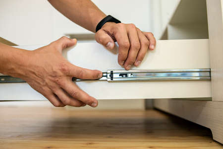 Close up of carpenter hands installing wooden drawer on sliding skids in contemporary cupboard cabinet.の写真素材
