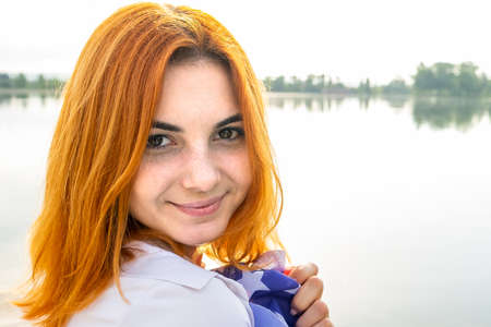 Portrait of happy smiling red haired girl. Positive young woman looking in camera outdoors.