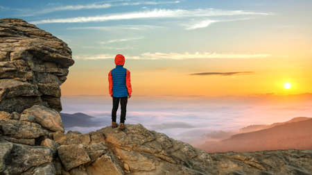 Young child boy hiker standing in mountains enjoying view of amazing mountain landscape at sunrise.の写真素材