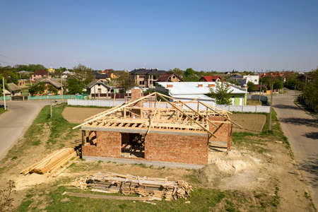 Aerial view of unfinished brick house with wooden roof frame structure under construction.