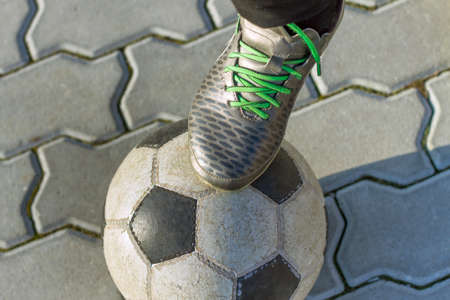 Close-up of boy foot in sport shoes on football ball outdoors on sunny pavement background. Vacations activity, sport and recreation concept.の写真素材