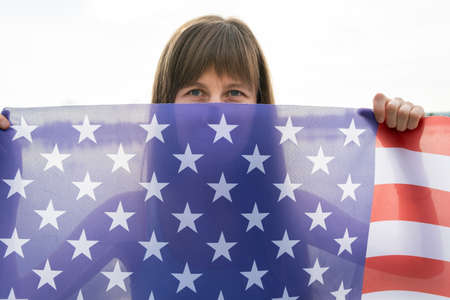 Portrait of happy smiling girl hiding her face behind USA national flag.