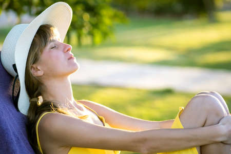 Young woman relaxing outdoors on sunny summer day. Happy lady lying down on comfortable beach chair daydreaming thinking. Calm beautiful smiling girl enjoying fresh air relaxing with closed eyes.の写真素材