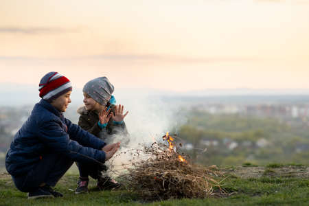 Two children playing with fire outdoors in cold weather.の写真素材