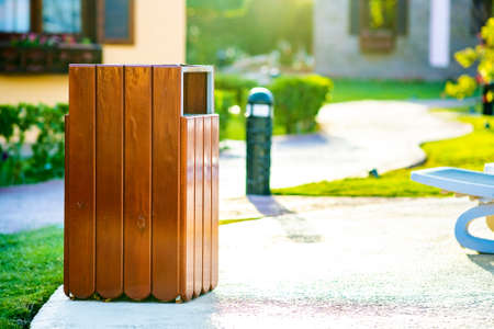 Yellow wooden trash can outdoors on the side of sidewalk in park. Garbage container on street outside .の写真素材