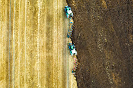 Aerial view of a tractor plowing black agriculture farm field after harvesting in late autumn.の写真素材