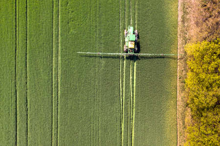 Tractor spraying chemical pesticides with sprayer on the large green agricultural field at spring.の写真素材