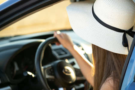 Driver woman in yellow straw hat sitting behind steering wheel driving a car. Summer vacation and travel concept.の写真素材