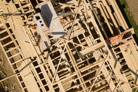 Aerial view of unfinished brick house with wooden roof frame structure under construction.