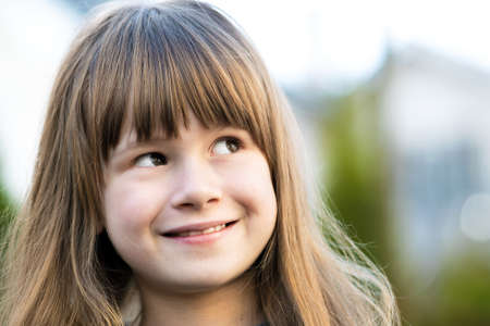 Portrait of pretty child girl with gray eyes and long fair hair smiling outdoors on blurred green bright background. Cute female kid on warm summer day outside.の写真素材