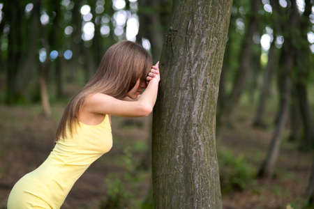 Young woman leaning to tree trunk in summer forest.の写真素材