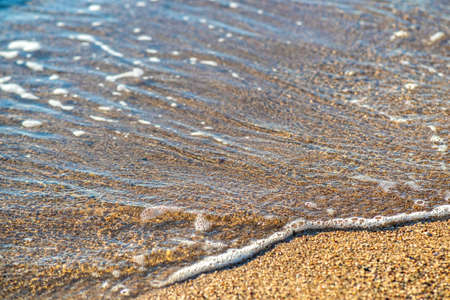 Close up of small sea waves with clear blue water over yellow sand beach at summer sunny shore.