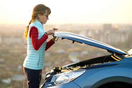 Young woman opening bonnet of broken down car having trouble with her vehicle. Female driver near auto with popped up hood.の写真素材
