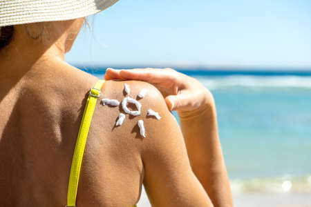 Back view of young woman tanning at the beach with sunscreen cream in sun shape on her shoulder. UV...
