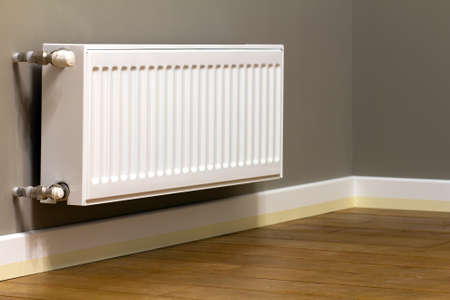 White metal heating radiator mounted on gray wall inside a room.の写真素材