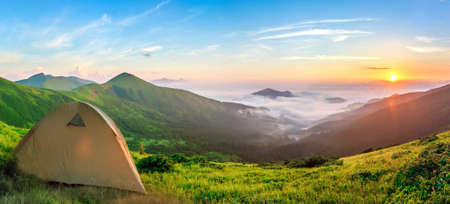 Tourist tent located in summer mountains at sunset. Hiking camp in evening nature. Travel and get away concept.の写真素材