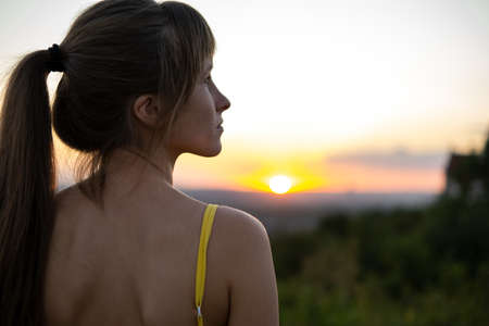 Young woman standing outdoors enjoying sunset view.の写真素材