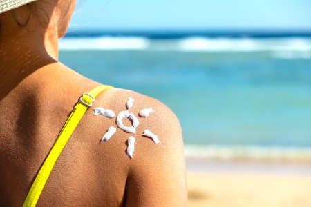 Back view of young woman tanning at the beach with sunscreen cream in sun shape on her shoulder. UV sunburn protection and sunblock skincare conceptの写真素材