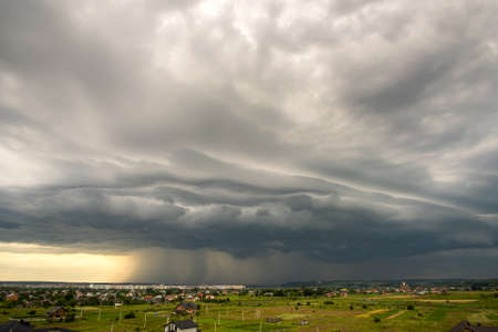 Moody landscape with dark stormy clouds with falling heavy downpour shower rain over distant town...