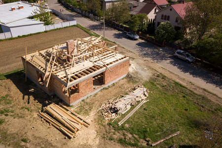 Aerial view of unfinished brick house with wooden roof frame structure under construction.