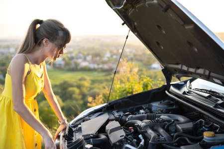 Puzzled female driver standing near her car with popped up hood looking at broken engine.の写真素材