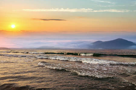 Beautiful sunrise in mountains with white fog below and crashing waves of lake water.の写真素材