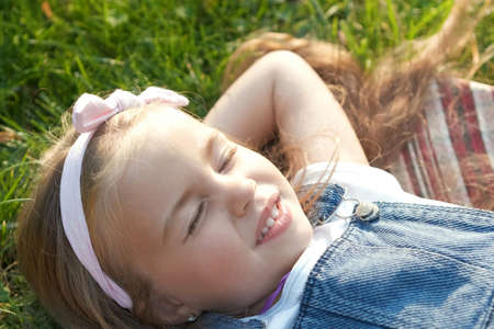 Pretty little child girl laying down on green grass in summer taking a nap.の写真素材