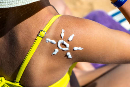 Back view of young woman tanning at the beach with sunscreen cream in sun shape on her shoulder. UV...