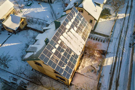 House roof covered with solar panels in winter with snow on top. Energy efficiency and maintenance...