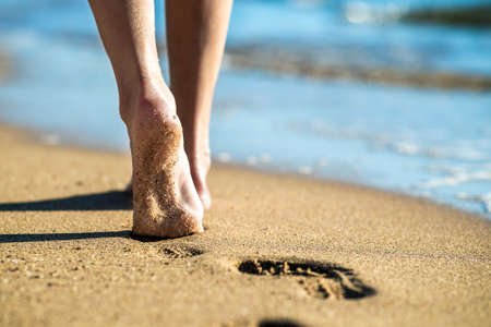 Close up of woman feet walking barefoot on sand leaving footprints on golden beach. Vacation, travel and freedom concept. People relaxing in summer.の写真素材
