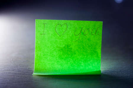 I love you message written on bright green sheet writing paper note with heart on blue background.