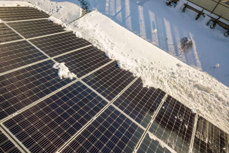 Close up surface of a house roof covered with solar panels in winter with snow on top. Energy...