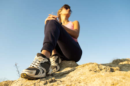 Woman hiker sitting on a steep big rock enjoying warm summer day. Young female climber resting during sports activity in nature. Active recreation in nature concept.の写真素材