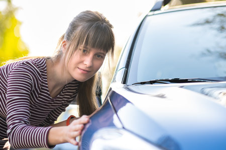 Young woman customer closely examining a new car at dealer outdoor shop before purchasing it.の写真素材